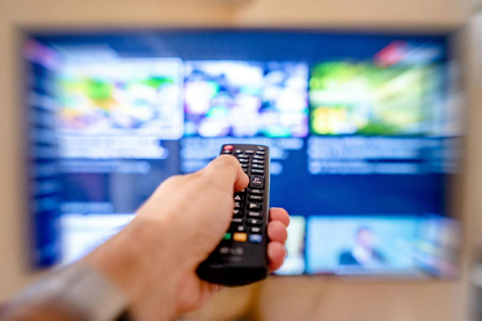 Person holding TV remote while browsing streaming service interface on large screen
