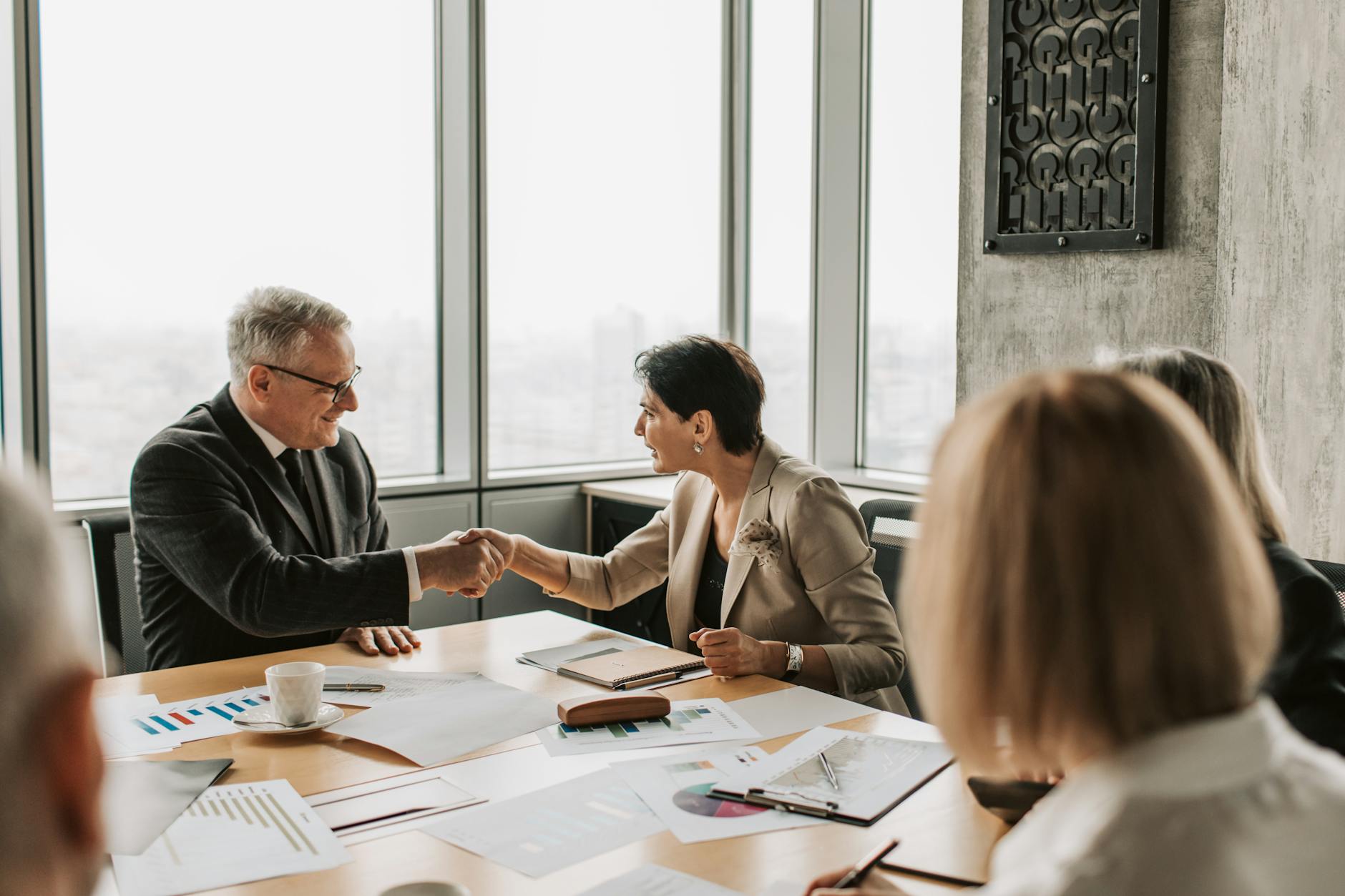 Business professionals shaking hands over documents during real estate transaction negotiation