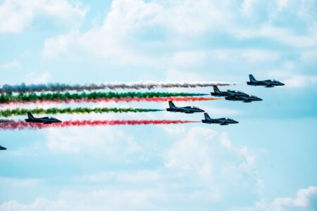 Military aircraft flying over conflict zone with smoke rising below