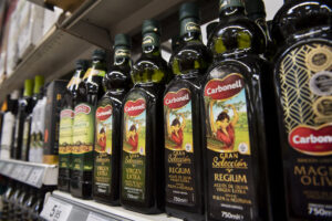Glass bottles of olive oil on a store shelf representing Deoleo's retail market presence