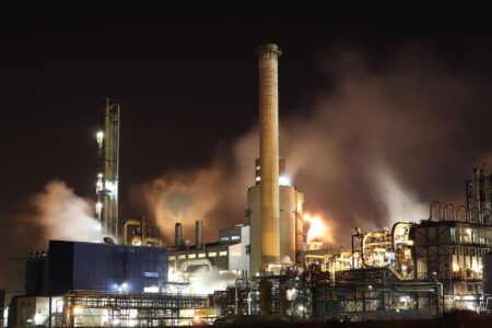 Industrial oil refinery with smoke rising against a cloudy sky