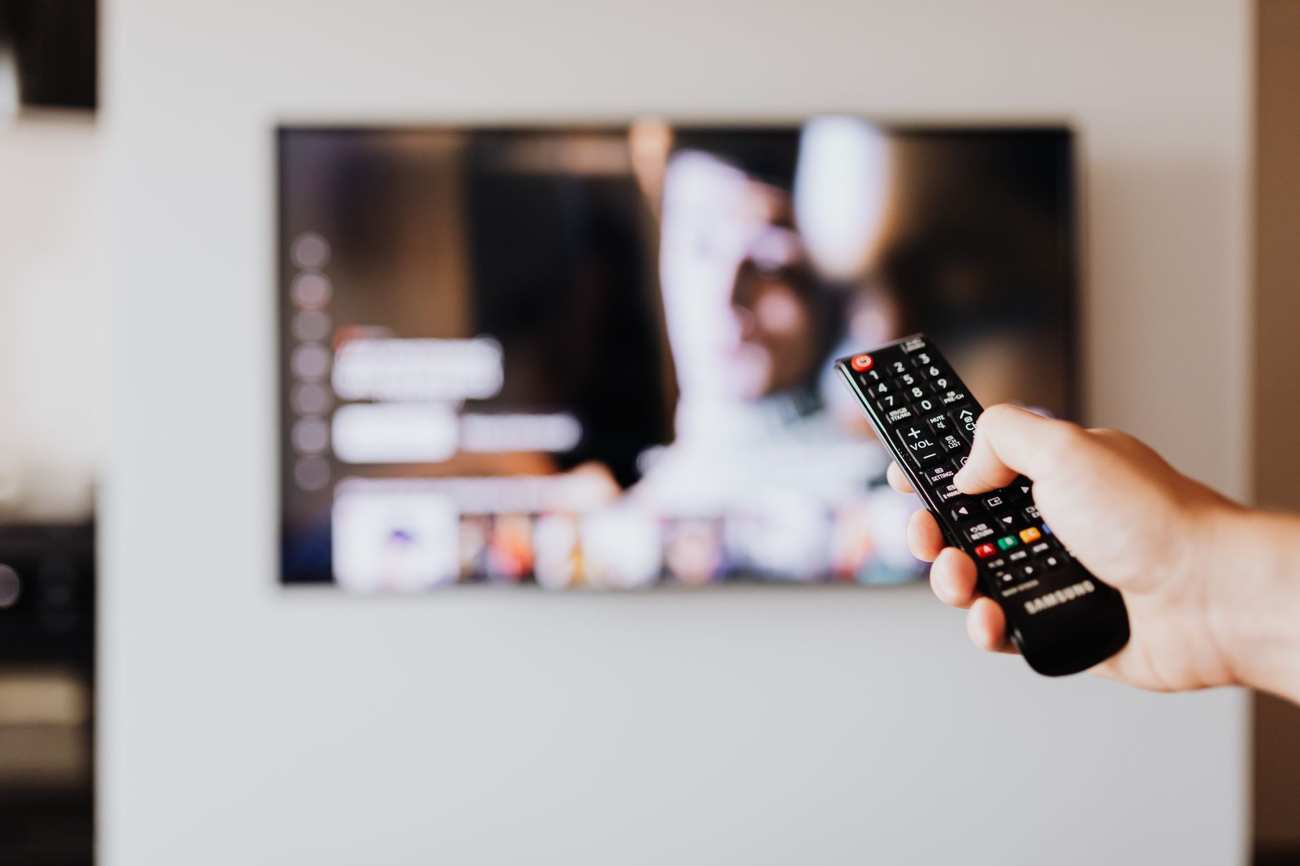Person holding a remote control in front of a streaming service on a television screen